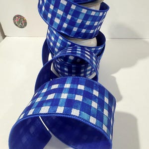 May include: A roll of blue and white checkered ribbon. The ribbon has a vibrant blue edge and a pattern of blue and white squares. The ribbon is unspooled, revealing the pattern and texture.