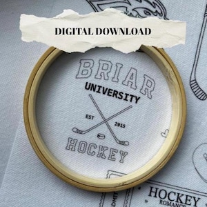 Könnte beinhalten: Ein runder Stickrahmen aus Holz umspannt weißen Stoff mit schwarzer Stickerei, die BRIAR UNIVERSITY HOCKEY EST 2015 und zwei gekreuzte Hockeyschläger zeigt. Darüber liegt ein zerrissener Papierstreifen mit dem Text DIGITAL DOWNLOAD.