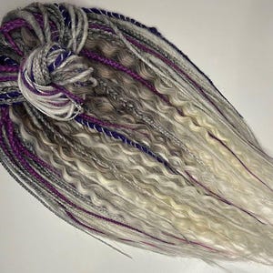 May include: A set of synthetic dreadlocks in shades of white, gray, and purple. The dreadlocks are long and wavy, with a variety of textures.