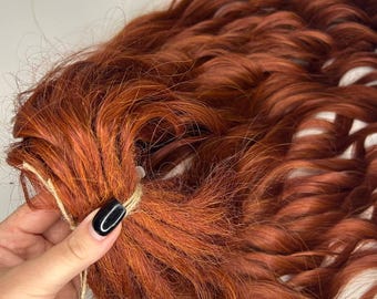 May include: A bundle of long, wavy, auburn-coloured human hair extensions. The hair is tied together with a brown string.
