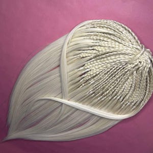 Op de afbeelding: Een lange, blonde haarverlenging met meerdere vlechten. De vlechten zijn aan het einde aan elkaar gebonden met een wit touwtje.