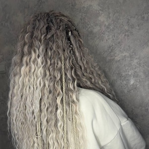 May include: A person with long, wavy, light grey hair with white braids. The person is wearing a white sweatshirt.