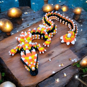 Puede incluir: Una escultura de dragón caprichosa hecha de caramelos de maíz, con una base y acentos negros. El cuerpo del dragón está adornado con caramelos de maíz naranjas, amarillos y blancos, creando un diseño festivo. La escultura se exhibe sobre una superficie de madera.