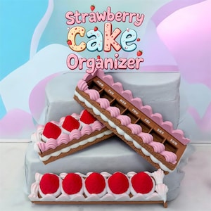 May include: A whimsical strawberry cake organizer with the text "Strawberry Cake Organizer". The organizer is designed to resemble a slice of cake, featuring pink frosting, white cream, and red strawberry toppings. It has compartments labeled for each day of the week.