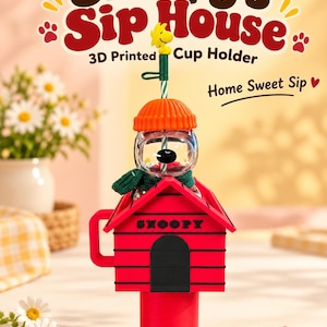 May include: A 3D printed cup holder shaped like a red doghouse with the word SNOOPY printed on the front. It features a clear spherical container with a green scarf, an orange beanie, and a yellow bird figure on top of a green and white straw.