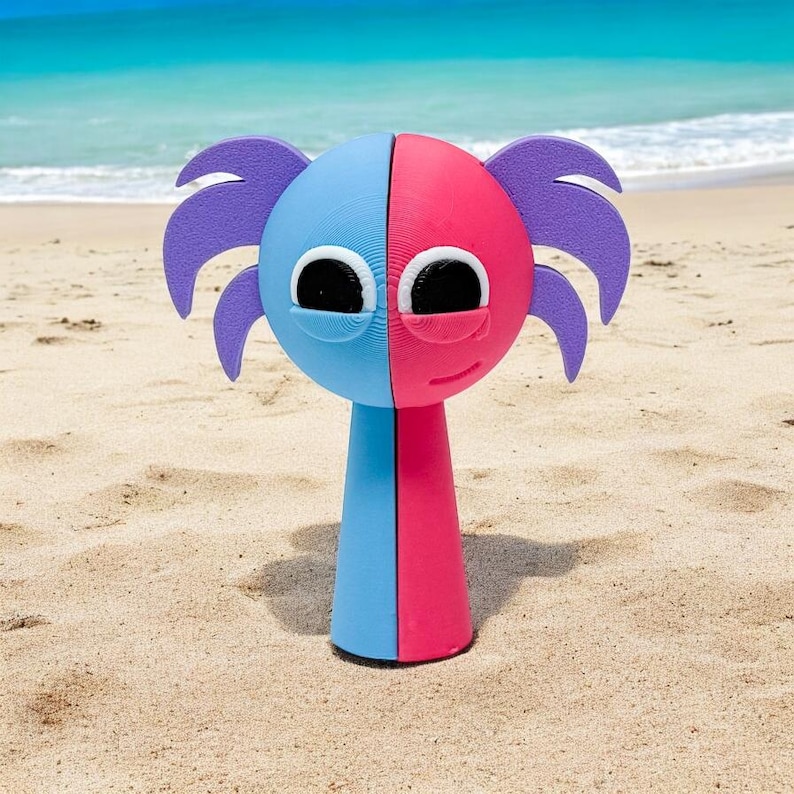 Puede incluir: Un juguete azul y rosa con una cara y pelo morado de pie en una playa de arena.