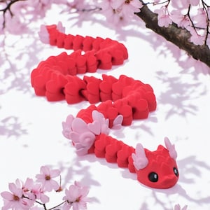 May include: A red and pink segmented dragon made of plastic. The dragon is curled up on a white surface with pink flowers in the background.