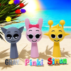 Puede incluir: Tres figuritas coloridas sobre un fondo de playa de arena. Una figurita gris que parece un gato con ojos grandes, una figurita rosa que parece un conejo con un lazo, y una figurita amarilla que parece un extraterrestre con ojos grandes. Las figuritas est&aacute;n etiquetadas como "Gray", "Pinki" y "Simon".