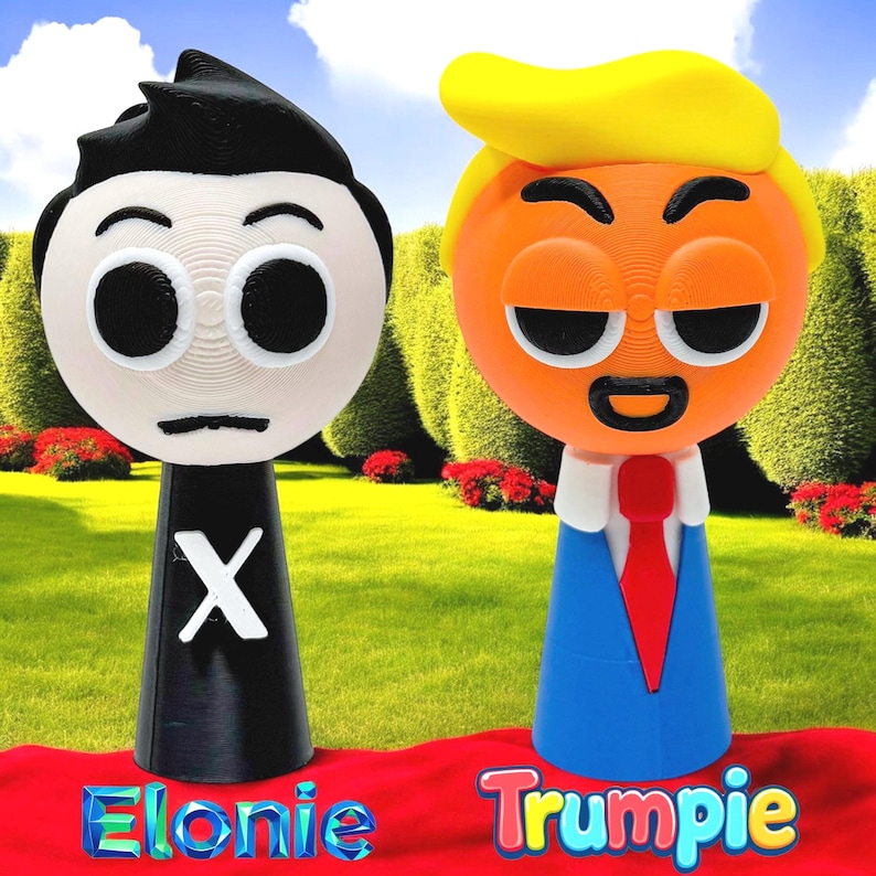 Puede incluir: Dos figuras impresas en 3D, una negra con una X blanca en el pecho y la otra naranja con un traje azul y una corbata roja. Las figuras est&aacute;n de pie sobre una superficie roja con las palabras "Elonie" y "Trumppie" escritas debajo.