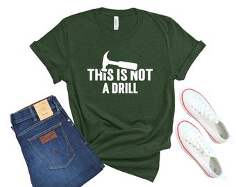 Op de afbeelding: Een groen T-shirt met een witte hamer en de tekst "Dit is geen oefening".