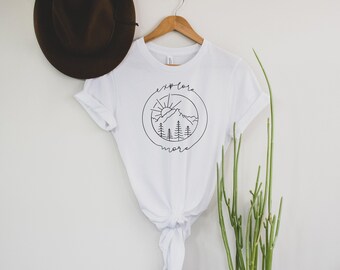 May include: White t-shirt with a black graphic of a mountain range, sun, and trees inside a circle with the text "explore more".