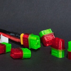 May include: Close-up of six green and red connector plugs. The plugs are made of plastic and have a rectangular shape. The plugs are arranged in a random pattern on a black surface.
