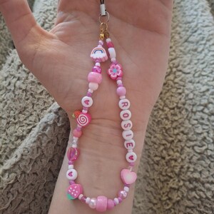 Handmade pink phone charm that is fully customisable. Each pink Y2K phone charm is made from upcycled pink beads, personalised with your name. Each custom phone charm is unique and makes a great gift for her, perfect for the Y2K trend. The pink phone straps are super cute and personalised, making a great Y2K phone accessory. The beaded pink phone wristlet is a great Y2K phone charm for any pink lover.