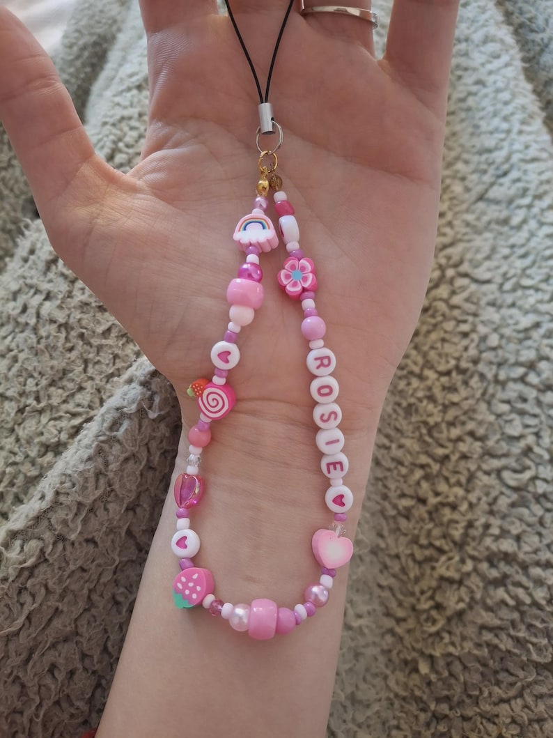 Handmade pink phone charm that is fully customisable. Each pink Y2K phone charm is made from upcycled pink beads, personalised with your name. Each custom phone charm is unique and makes a great gift for her, perfect for the Y2K trend. The pink phone straps are super cute and personalised, making a great Y2K phone accessory. The beaded pink phone wristlet is a great Y2K phone charm for any pink lover.