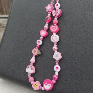 Handmade pink phone charm that is fully customisable. Each pink Y2K phone charm is made from upcycled pink beads, personalised with your name. Each custom phone charm is unique and makes a great gift for her, perfect for the Y2K trend. The pink phone straps are super cute and personalised, making a great Y2K phone accessory. The beaded pink phone wristlet is a great Y2K phone charm for any pink lover.