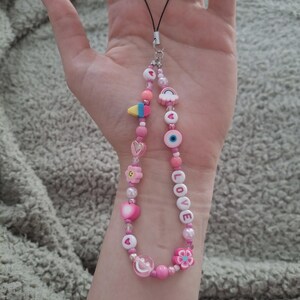 Handmade pink phone charm that is fully customisable. Each pink Y2K phone charm is made from upcycled pink beads, personalised with your name. Each custom phone charm is unique and makes a great gift for her, perfect for the Y2K trend. The pink phone straps are super cute and personalised, making a great Y2K phone accessory. The beaded pink phone wristlet is a great Y2K phone charm for any pink lover.