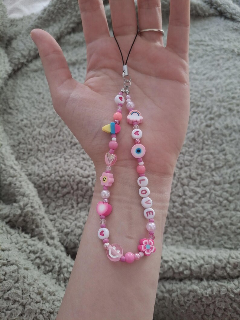 Handmade pink phone charm that is fully customisable. Each pink Y2K phone charm is made from upcycled pink beads, personalised with your name. Each custom phone charm is unique and makes a great gift for her, perfect for the Y2K trend. The pink phone straps are super cute and personalised, making a great Y2K phone accessory. The beaded pink phone wristlet is a great Y2K phone charm for any pink lover.