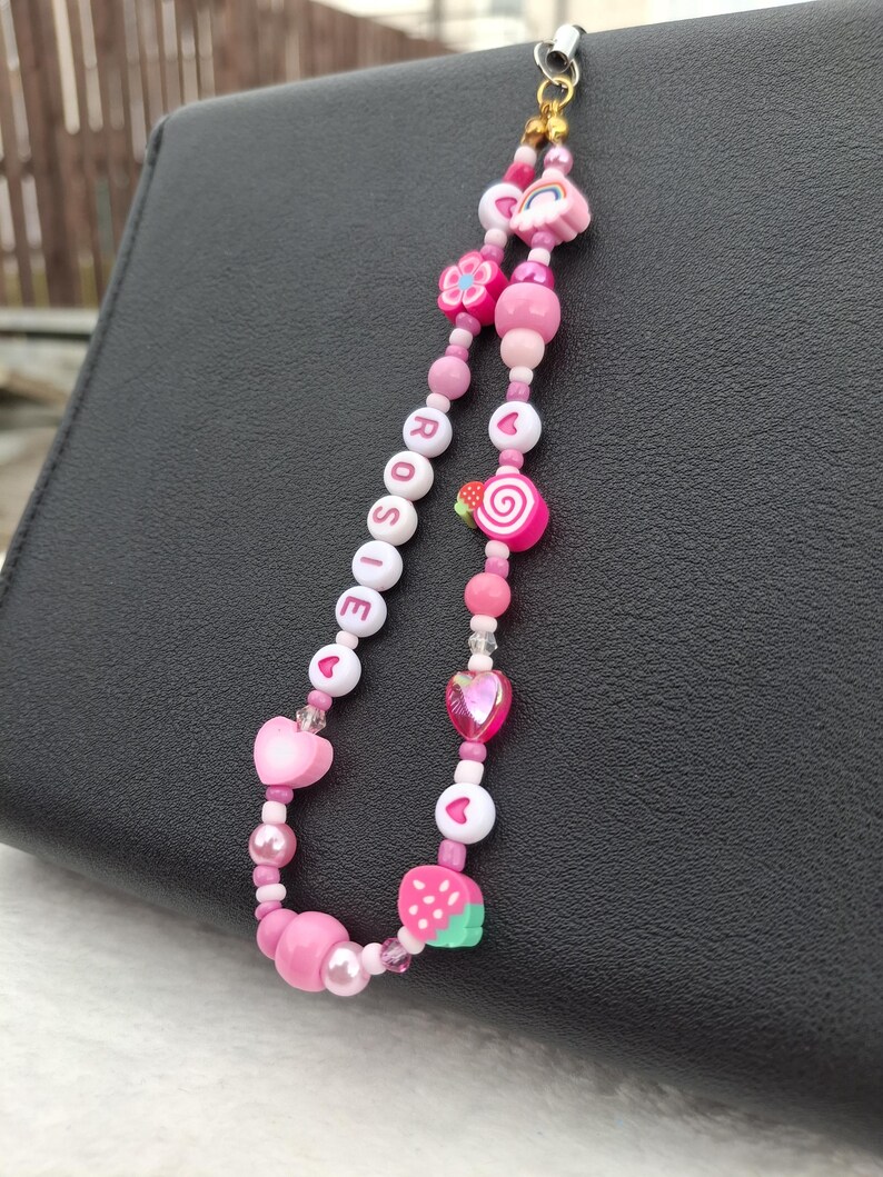 Handmade pink phone charm that is fully customisable. Each pink Y2K phone charm is made from upcycled pink beads, personalised with your name. Each custom phone charm is unique and makes a great gift for her, perfect for the Y2K trend. The pink phone straps are super cute and personalised, making a great Y2K phone accessory. The beaded pink phone wristlet is a great Y2K phone charm for any pink lover.