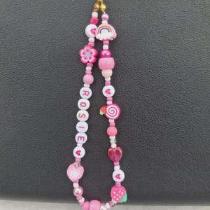 Handmade pink phone charm that is fully customisable. Each pink Y2K phone charm is made from upcycled pink beads, personalised with your name. Each custom phone charm is unique and makes a great gift for her, perfect for the Y2K trend. The pink phone straps are super cute and personalised, making a great Y2K phone accessory. The beaded pink phone wristlet is a great Y2K phone charm for any pink lover.