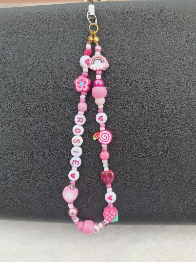 Handmade pink phone charm that is fully customisable. Each pink Y2K phone charm is made from upcycled pink beads, personalised with your name. Each custom phone charm is unique and makes a great gift for her, perfect for the Y2K trend. The pink phone straps are super cute and personalised, making a great Y2K phone accessory. The beaded pink phone wristlet is a great Y2K phone charm for any pink lover.