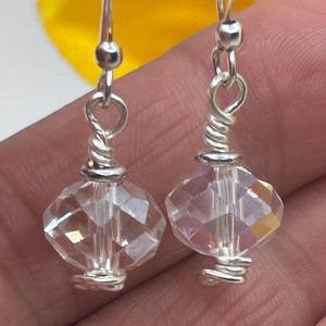 May include: A pair of clear crystal earrings with silver-colored metal accents. The earrings feature faceted, diamond-shaped crystals suspended from a silver wire. The crystals reflect light, creating a sparkling effect. The earrings are designed for pierced ears.