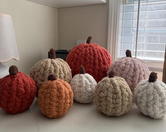 May include: A collection of handmade, plush pumpkins in various sizes and colors, including orange, red, tan, white, and pink. Each pumpkin has a brown stem, perfect for fall decor.