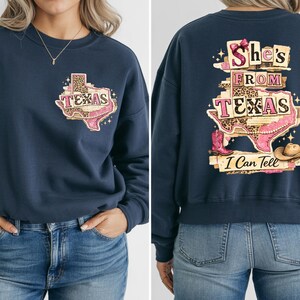 Może przedstawiać: Granatowa bluza z grafiką w kształcie Teksasu. Prz&oacute;d z napisem "Texas" z r&oacute;żowym i lampartowym wzorem. Tył z napisem "She's From Texas I Can Tell" z butem i kapeluszem kowbojskim. Swobodny top.