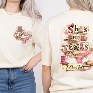 Może przedstawiać: Kremowa koszulka z grafiką w kształcie Teksasu, r&oacute;żowym butem kowbojskim i napisem "Texas". Tył koszulki przedstawia napis "She's From Texas I Can Tell" z butem kowbojskim i kapeluszem.