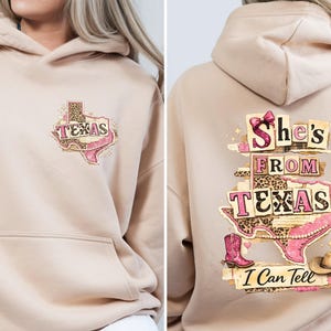 Może przedstawiać: Beżowa bluza z kapturem z przednią kieszenią i kapturem. Prz&oacute;d przedstawia grafikę w kształcie Teksasu ze słowem "Texas" i wzorem w cętki. Tył bluzy z kapturem ma napis "She's From Texas I Can Tell" z r&oacute;żowym butem, kapeluszem i grafiką Teksasu.