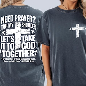 May include: Dark gray t-shirt with a white cross graphic on the front and back. The back of the shirt features the text "NEED PRAYER? TAP MY SHOULDER, LET'S TAKE IT TO GOD TOGETHER" and a Bible verse. A casual, comfortable tee.
