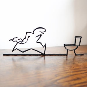 May include: A quirky black metal sculpture showing a cartoon figure sprinting towards a toilet. The figure is formed from angular lines with a cloud, implying movement. The toilet is a simple outline, creating a humorous scene.