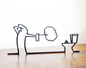 May include: A black and white line art sculpture of a person lifting a toilet brush. The sculpture is set on a wooden surface, against a white backdrop. The toilet is also rendered in black and white.
