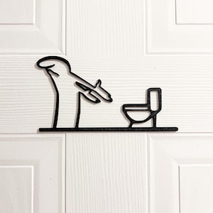 Peut inclure: Panneau de salle de bain en métal noir représentant un bonhomme allumette visant des toilettes avec un pistolet. Le panneau est monté sur une porte blanche à surface texturée. Un article humoristique et décoratif.