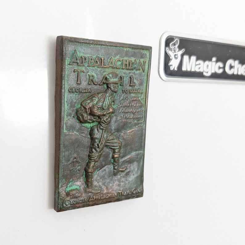 May include: A green and brown metal plaque with a raised image of a hiker on the Appalachian Trail. The plaque reads "Appalachian Trail Georgia to Maine".