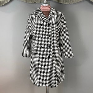 May include: A black and white houndstooth pattern coat with a double-breasted design. The coat has a classic collar, long sleeves, and black buttons. The coat is displayed on a mannequin.