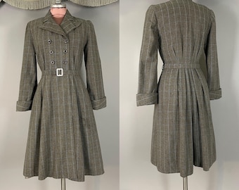May include: A double-breasted grey coat featuring a white windowpane check pattern, a notched collar, and a belted waist with a silver buckle. The coat has long sleeves with folded cuffs and a pleated skirt that falls below the knee.
