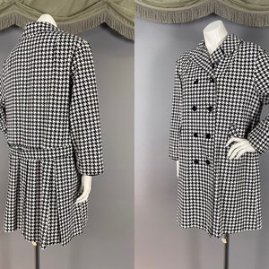 May include: A black and white houndstooth pattern coat with a double-breasted design. The coat features a pleated skirt and long sleeves. The coat is displayed on a mannequin.