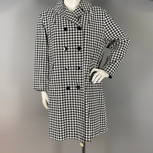May include: A black and white houndstooth pattern coat with a double-breasted design. The coat has black buttons and a black trim on the collar and cuffs. The coat is displayed on a mannequin.