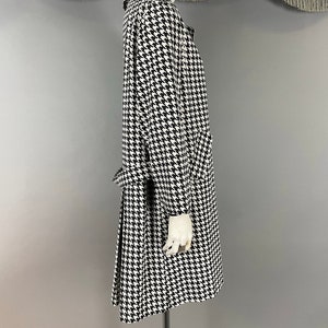May include: A black and white houndstooth pattern coat with a collar, long sleeves, and a belt. The coat is displayed on a mannequin. The coat has a classic design and appears to be made of a medium-weight fabric.