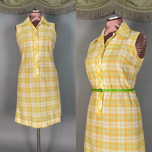 May include: A sleeveless collared dress featuring a yellow, white, and light green plaid pattern. The dress has a button-down front placket and is shown both without and with a thin, bright green belt cinched at the waist on a mannequin.