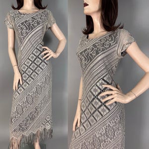 May include: A vintage, floor-length dress with a unique design. The dress features a combination of patterned lace and diagonal stripes in shades of gray and black. The dress has short sleeves and a fringe hemline.