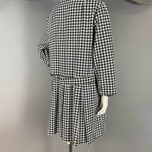 May include: A black and white houndstooth dress and jacket ensemble. The dress has a pleated skirt and fitted waist, while the jacket features long sleeves and a collar. The outfit is displayed on a mannequin.