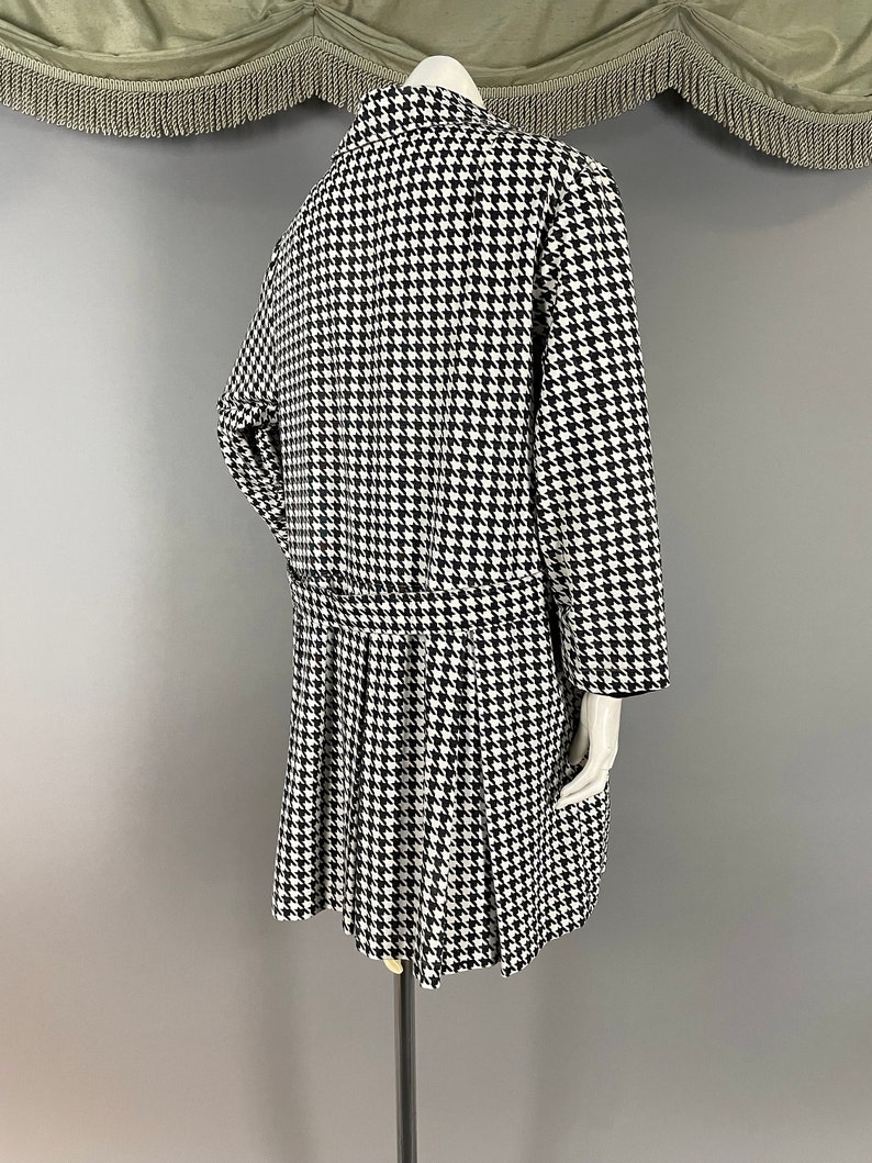 May include: A black and white houndstooth dress and jacket ensemble. The dress has a pleated skirt and fitted waist, while the jacket features long sleeves and a collar. The outfit is displayed on a mannequin.