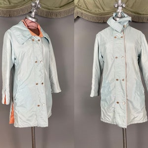 May include: A light blue vintage coat with a double-breasted design and gold-colored buttons. The coat has a contrasting peach-colored lining and trim. The coat is displayed on a mannequin.