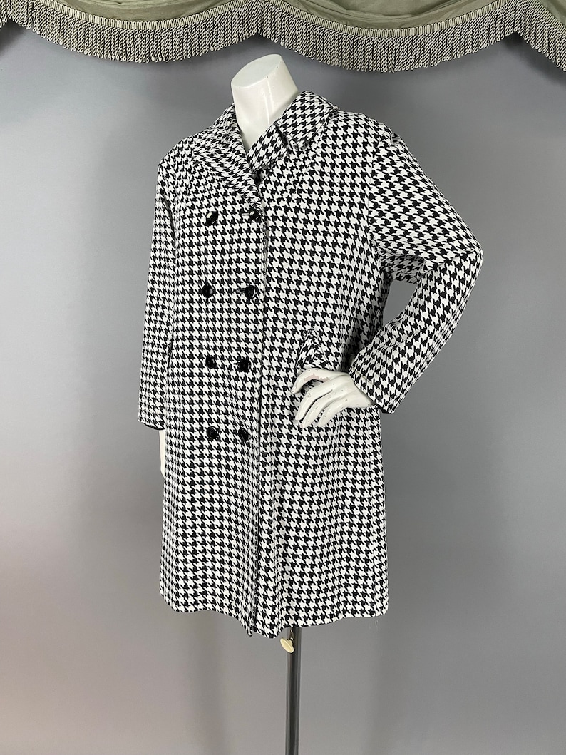 May include: A black and white houndstooth coat with a double-breasted design. The coat features a classic collar and long sleeves. The coat is displayed on a mannequin.
