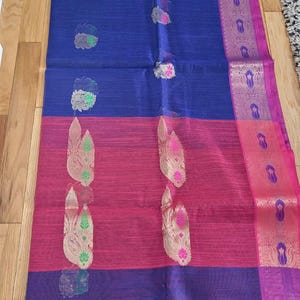 May include: A colourful textile with a block design. The top section is a deep blue, transitioning to a bright pink, and ending with a purple section. The fabric is decorated with ornate, floral-like patterns in gold, green, and pink. A decorative border runs along the edge.