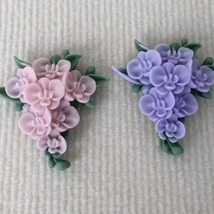 May include: Two clusters of artificial flowers, one in pink and one in purple, with green leaves. The flowers are shaped like orchids.