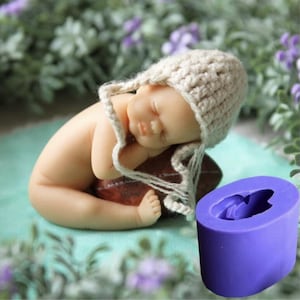 May include: Purple silicone mold for making a sleeping baby cake topper. The mold is shaped like a baby with a hat and is lying on its side.