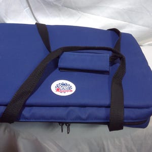May include: A navy blue insulated cooler bag with black straps and a handle. The bag has a zip closure and a circular logo on the front. The bag is designed for carrying food and drinks, ideal for picnics.