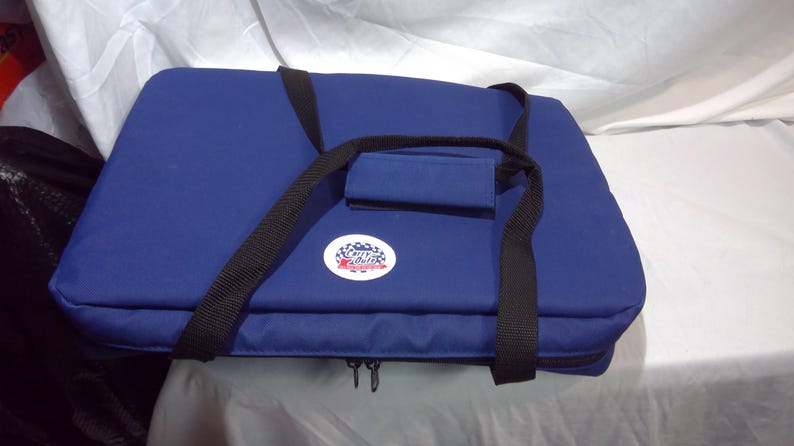 May include: A navy blue insulated cooler bag with black straps and a handle. The bag has a zip closure and a circular logo on the front. The bag is designed for carrying food and drinks, ideal for picnics.
